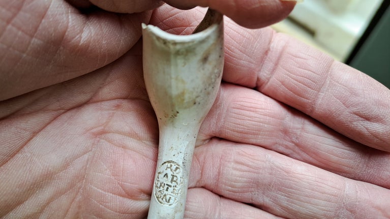 A nearly complete clay pipe being held in the palm of a hand. On the pipe you can see the makers mark RW Carpenter